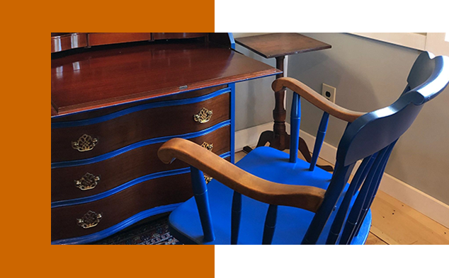 A blue chair and desk in front of a dresser.