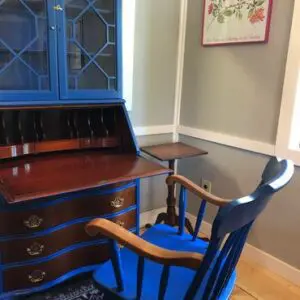 A blue chair and desk in front of a wooden dresser.