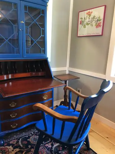 A blue chair and desk in front of a wooden dresser.