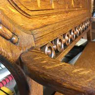 A close up of the wooden seat and back of an old piano.